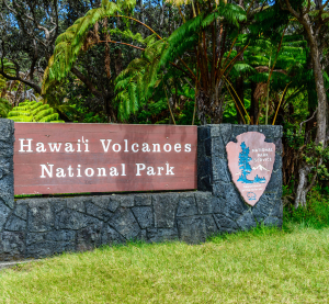 Eingangsschild des Hawaii-Volcanoes-Nationalparks, umgeben von dichter tropischer Vegetation.