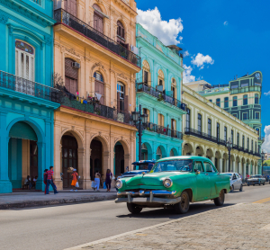 Klassischer Oldtimer f&auml;hrt an bunten Kolonialgeb&auml;uden in Havanna, Kuba, bei blauem Himmel vorbei.