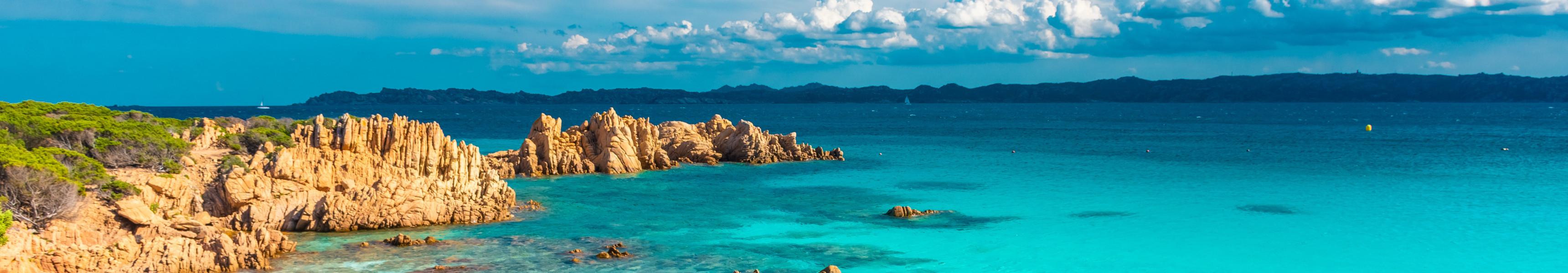 Traumstrand mit t&uuml;rkisblauem Wasser und r&ouml;tlichen Felsen auf Sardinien.