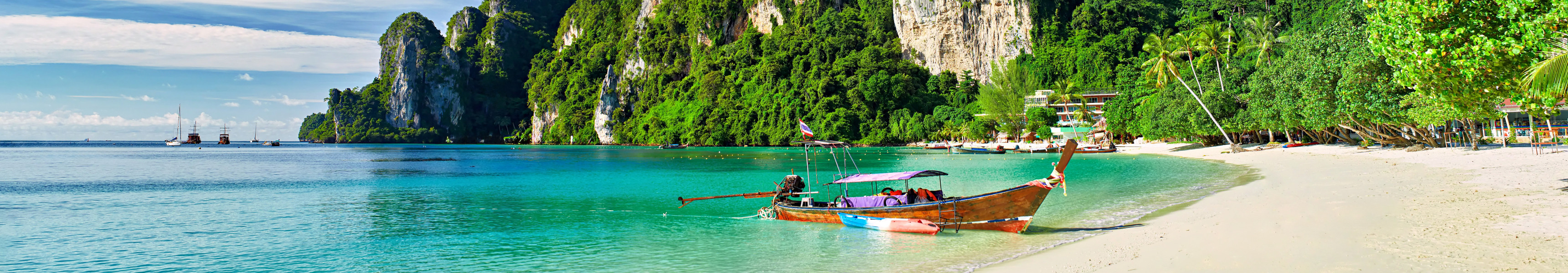 Tropischer Strand mit wei&szlig;em Sand und t&uuml;rkisfarbenem Wasser, im Vordergrund ein traditionelles Longtailboot