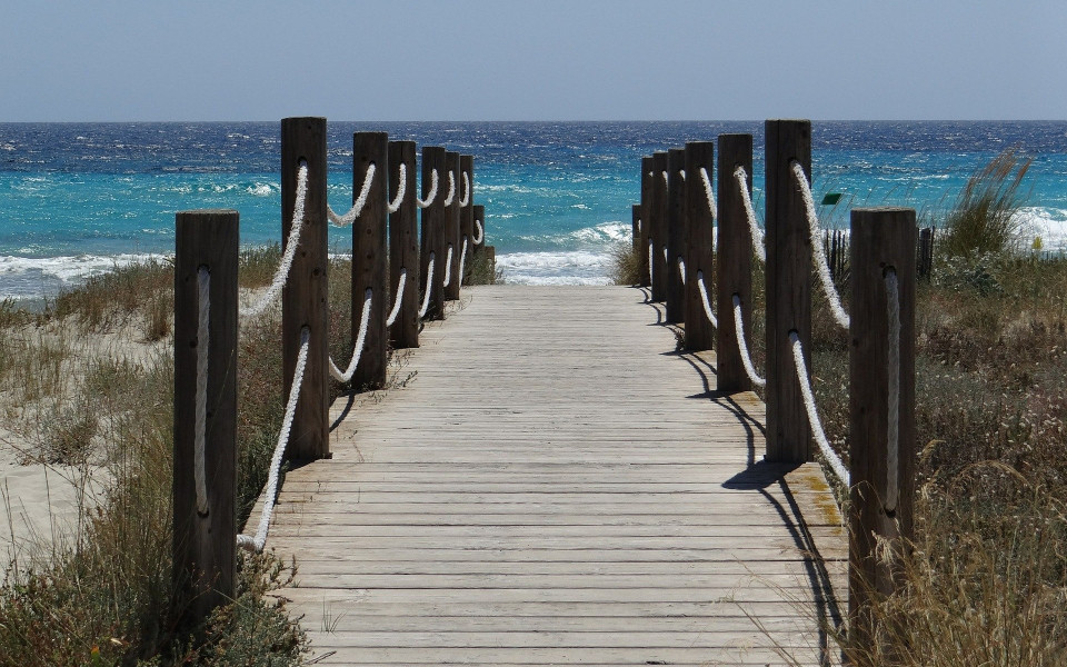 Ein Holzsteg f&uuml;hrt vom Land zum Meer, mit Blick auf das azurblaue Wasser von Menorca.