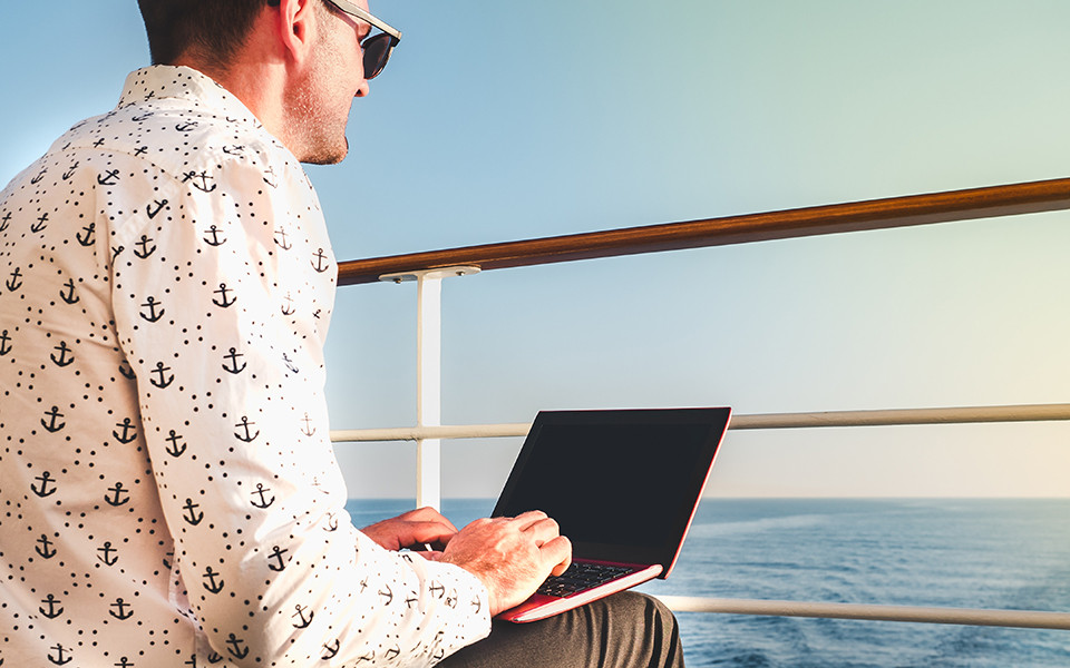 Mann mit Laptop und Sonnenbrille auf dem Deck eines Kreuzfahrtschiffs