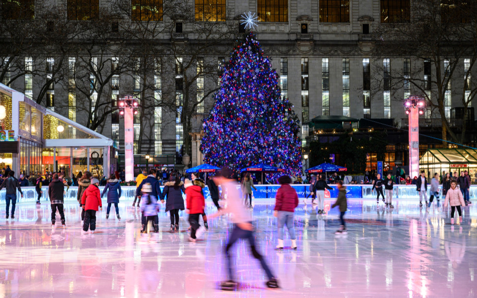 Eisbahn im Bryant Park mit funkelndem Weihnachtsbaum und fr&ouml;hlichen Menschen in winterlicher Atmosph&auml;re mitten in New York City.