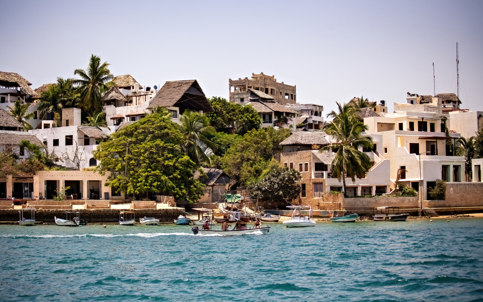Die K&uuml;ste von Lamu in Kenia mit traditionellen H&auml;usern und Fischerbooten am Wasser.