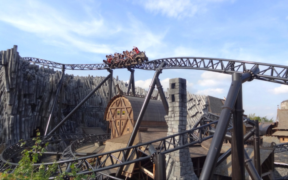 Achterbahn im Phantasialand, mit Fahrg&auml;sten, die &uuml;ber eine kurvige Strecke nahe einem thematisierten Geb&auml;ude fahren.