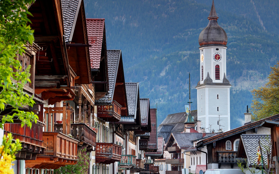 Die Ludwigsstra&szlig;e in Partenkirchen mit traditionellen bayerischen H&auml;usern und Balkonen und im Hintergrund der Zwiebelturm der Pfarrkirche St. Anton vor alpiner Bergkulisse.