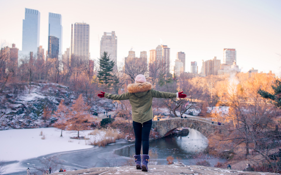 Person mit Winterjacke und M&uuml;tze blickt &uuml;ber verschneiten Central Park in New York City mit Skyline im Hintergrund