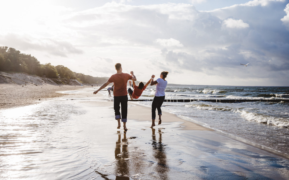 Familie l&auml;uft am Strand entlang und spielen mit ihrem Kind